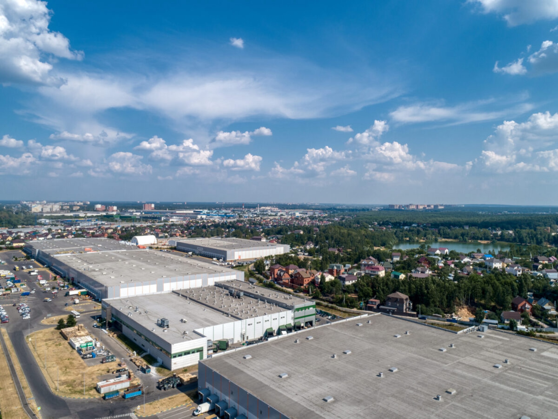 Huge warehouse building with flat roof and cars on parking site under blue sky with fluffy clouds near city in summer bird eye view