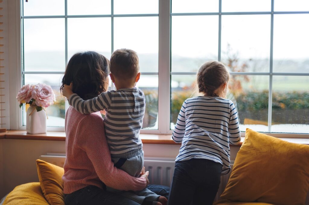 mother and two children looking through window at quarantine time