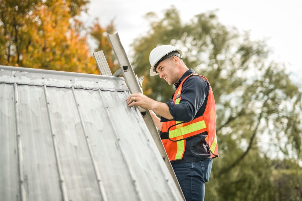 A man with hard hat standing on steps inspecting house roof
