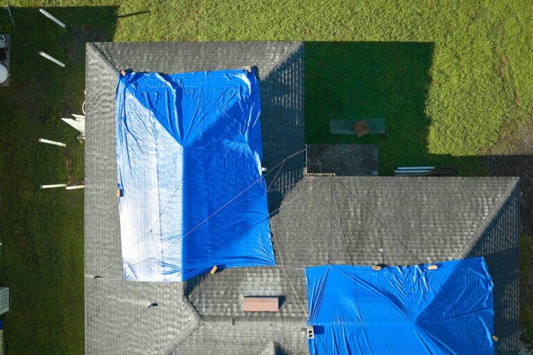 Top view of leaking house roof covered with protective tarp sheets against rain water leaks until replacement of asphalt shingles. Damage of building rooftop as aftermath of hurricane.