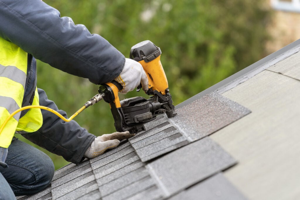 Workman using nail gun install tile on roof of new house 