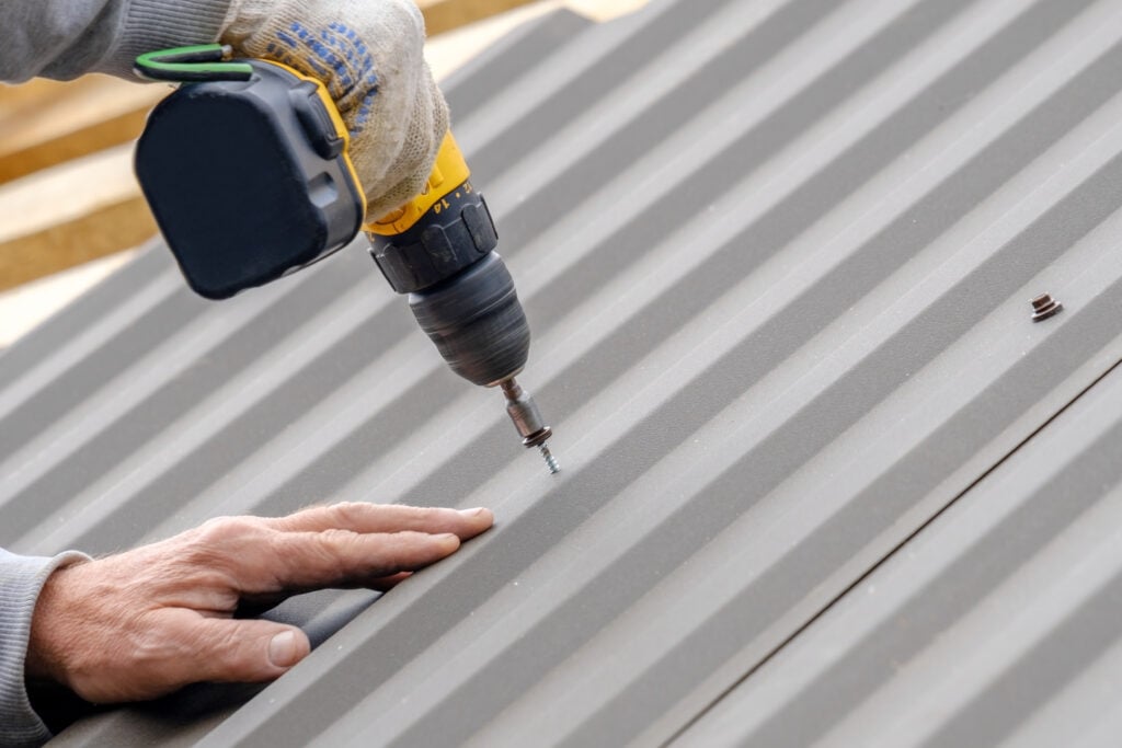 Worker in gloves with a screwdriver screw the roofing sheet on roof.