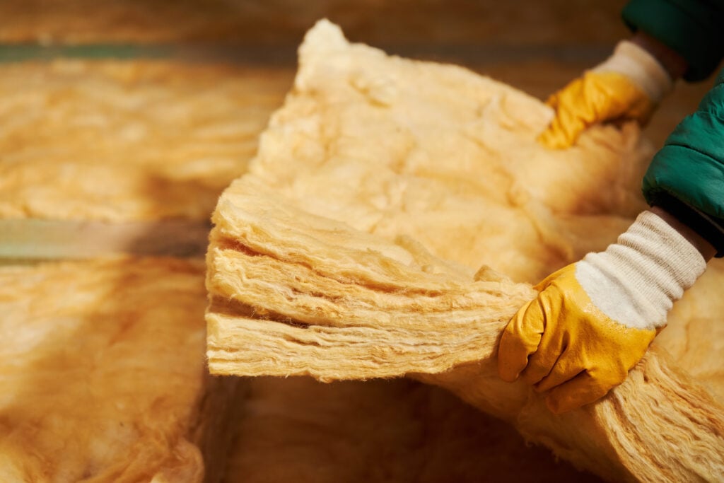 Construction worker thermally insulating house attic with glass