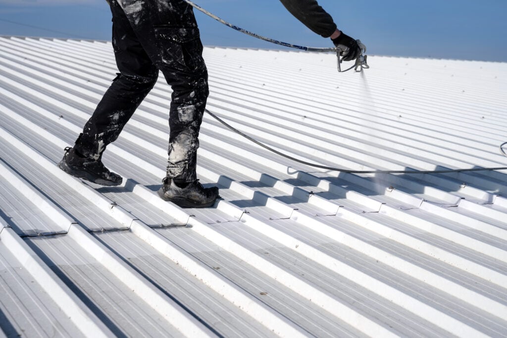 Metal roof painting. Technician performing painting of roof in white color.