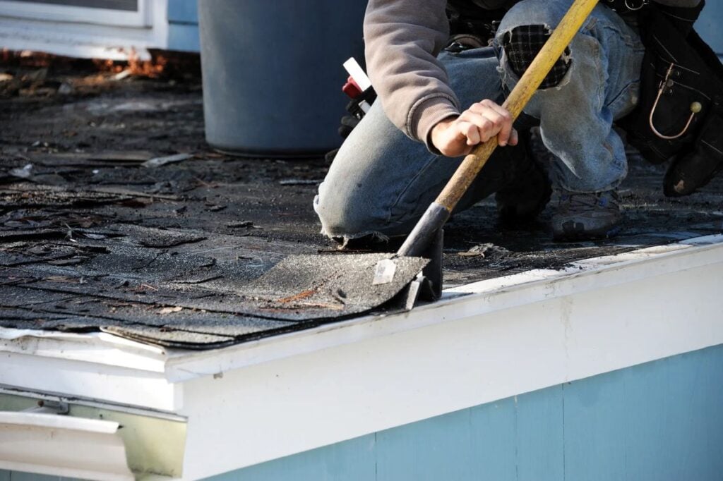 asphalt shingle roof replacement worker using shovel on bad shingles